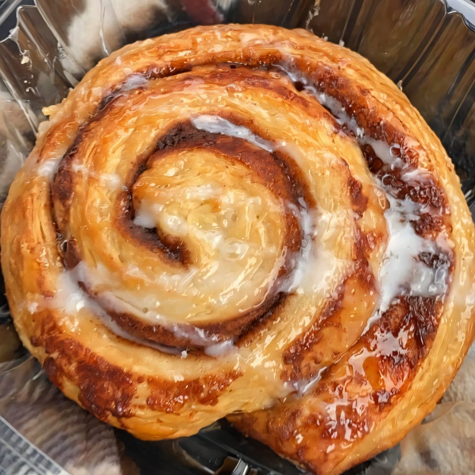 A close-up of a glazed cinnamon roll from Parma Market & Bakery, with white icing and a golden crust.