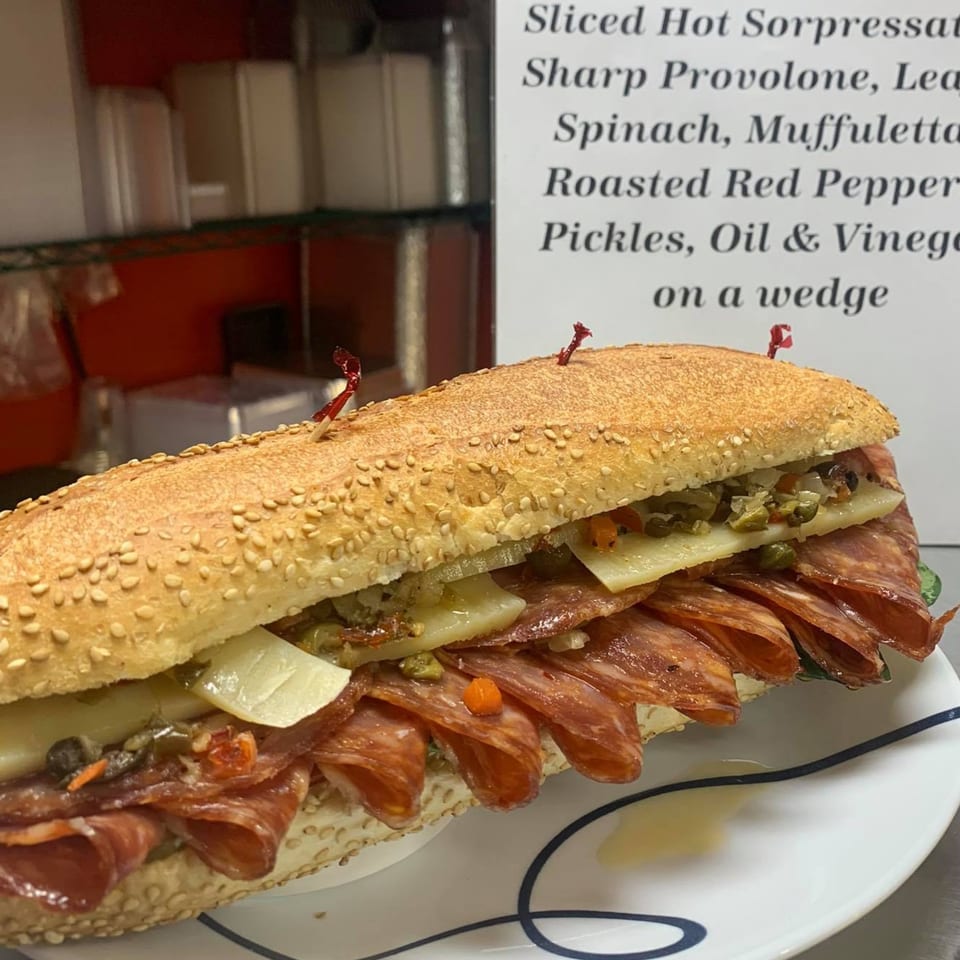 A deli sandwich on a sesame seed roll, filled with meats, cheese, and vegetables.