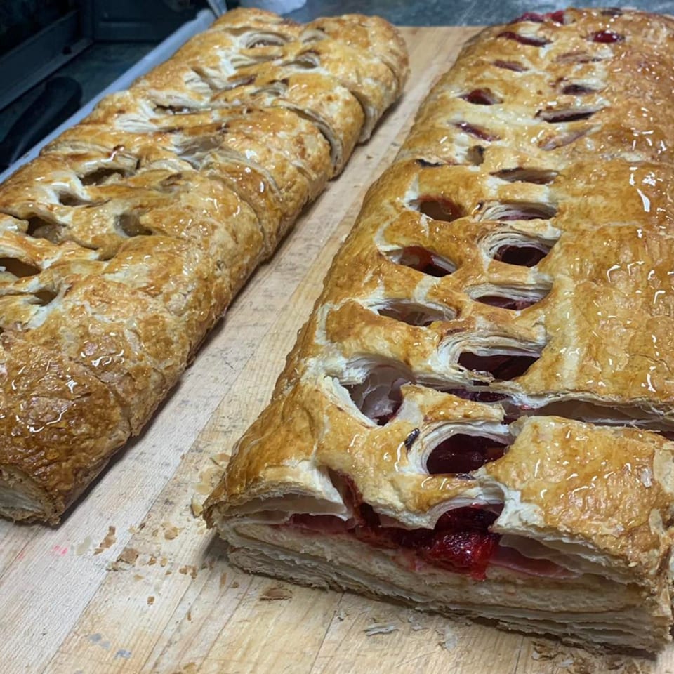 Two golden-brown pastries with fruit filling, one with cherry and the other with apple, on a wooden board.